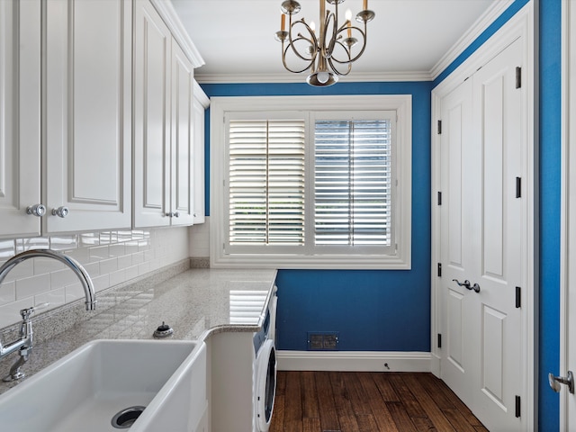 clothes washing area with an inviting chandelier, a sink, dark wood-style flooring, baseboards, and washer / clothes dryer