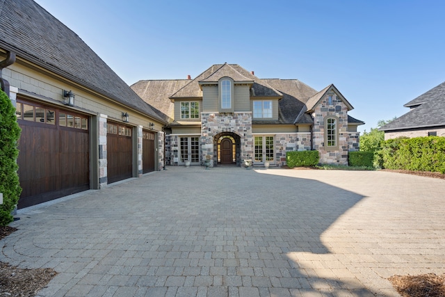 french country home with stone siding, decorative driveway, and an attached garage