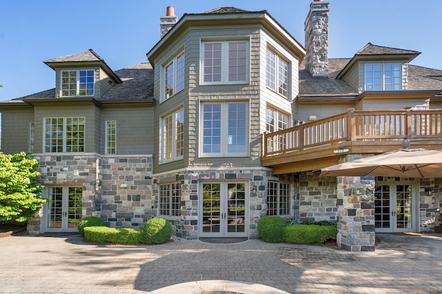 rear view of property featuring a chimney, french doors, and stone siding