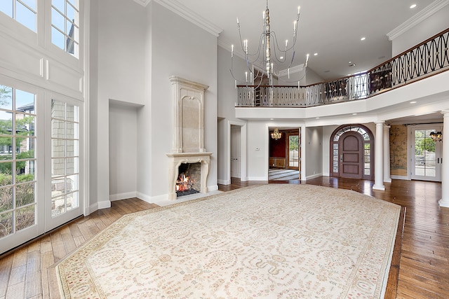 unfurnished living room with decorative columns, hardwood / wood-style flooring, baseboards, a notable chandelier, and a high ceiling