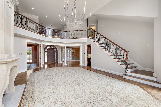 entryway with wood finished floors, an inviting chandelier, stairs, decorative columns, and a towering ceiling