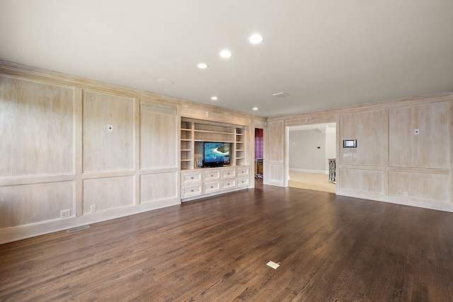 unfurnished living room with recessed lighting, built in features, dark wood-type flooring, visible vents, and a decorative wall