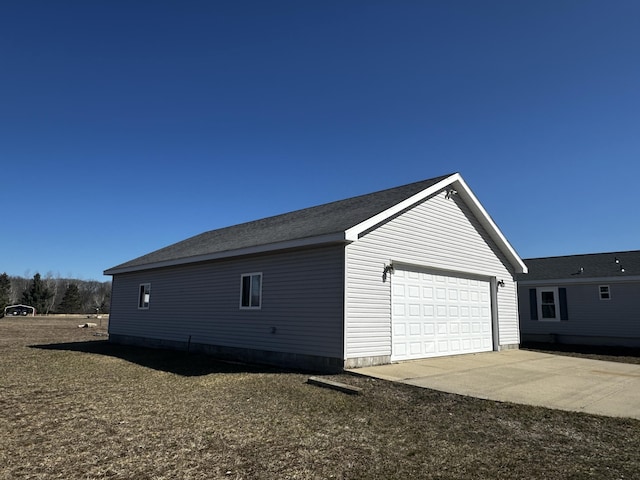view of home's exterior featuring an attached garage, a shingled roof, and an outbuilding