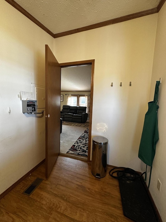 hallway with a textured ceiling, baseboards, ornamental molding, visible vents, and wood finished floors