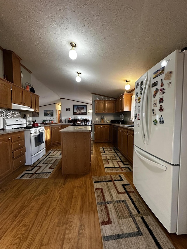 kitchen with a center island, wood finished floors, white appliances, under cabinet range hood, and vaulted ceiling
