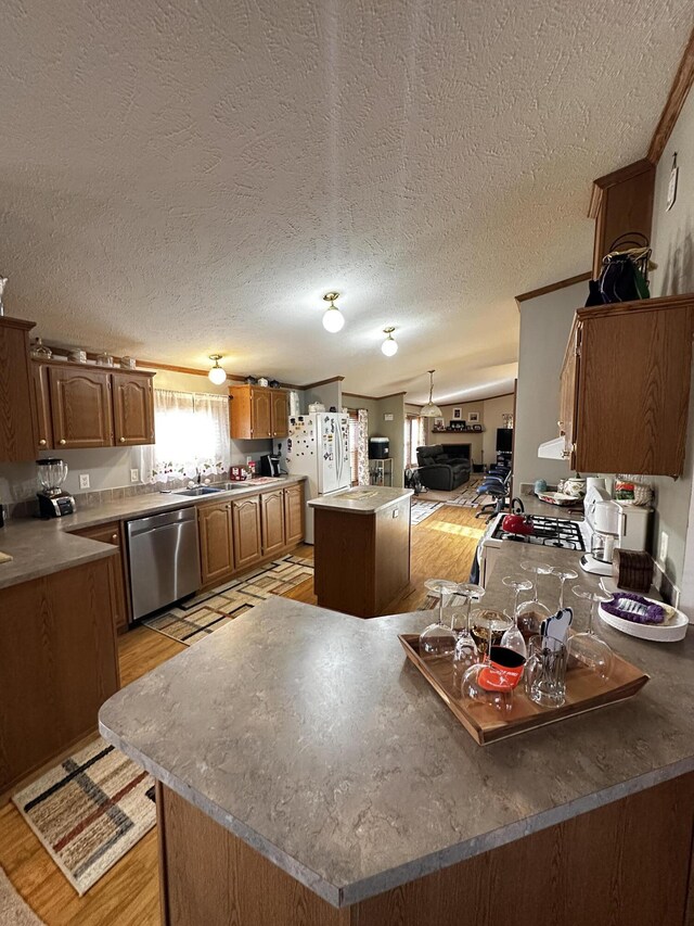 kitchen featuring freestanding refrigerator, a textured ceiling, dishwasher, a sink, and a kitchen island