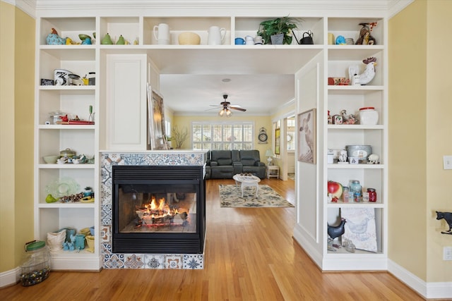 living area featuring light wood-type flooring, a ceiling fan, baseboards, and a fireplace