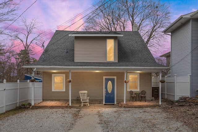 back of house at dusk featuring a porch, fence, and a shingled roof