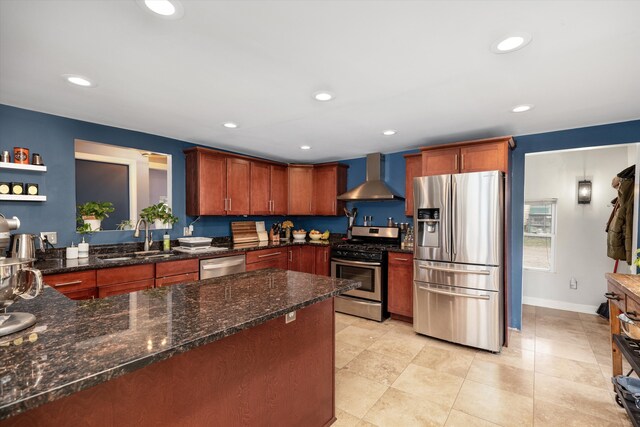 kitchen with dark stone countertops, recessed lighting, wall chimney exhaust hood, stainless steel appliances, and a sink