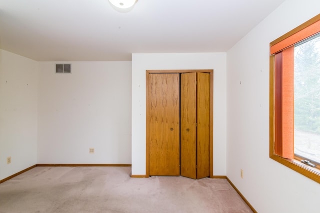 unfurnished bedroom with a closet, visible vents, light colored carpet, and baseboards