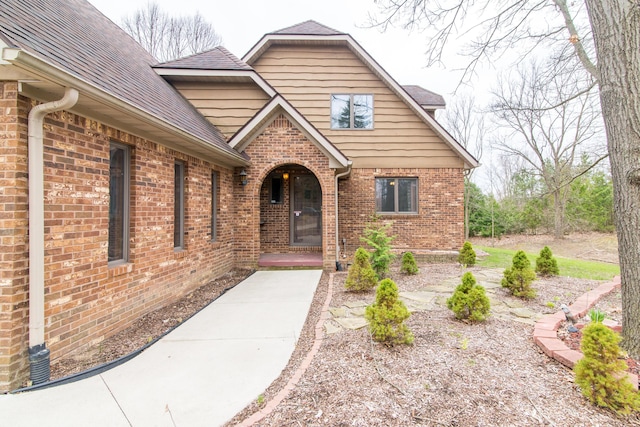 entrance to property featuring a shingled roof and brick siding