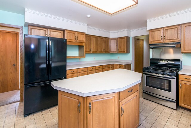 kitchen featuring stainless steel range with gas stovetop, freestanding refrigerator, under cabinet range hood, a kitchen island, and light tile patterned flooring