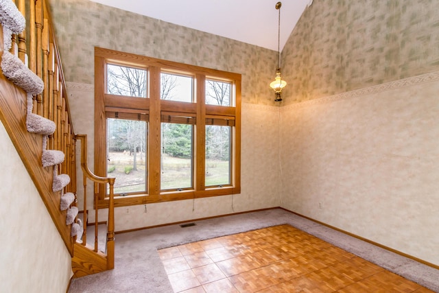 carpeted empty room featuring visible vents, lofted ceiling, plenty of natural light, and stairway