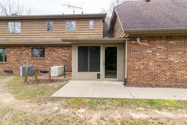 rear view of property with a shingled roof, a patio area, central AC unit, and brick siding