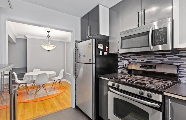 kitchen featuring hanging light fixtures, dark countertops, crown molding, stainless steel appliances, and decorative backsplash