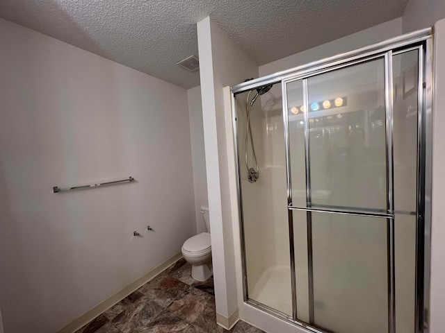 bathroom featuring a shower stall, toilet, baseboards, visible vents, and a textured ceiling