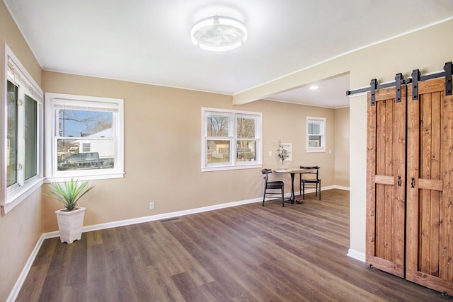 interior space featuring visible vents, baseboards, a barn door, and wood finished floors