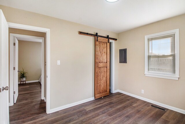 unfurnished bedroom with baseboards, dark wood finished floors, visible vents, and a barn door