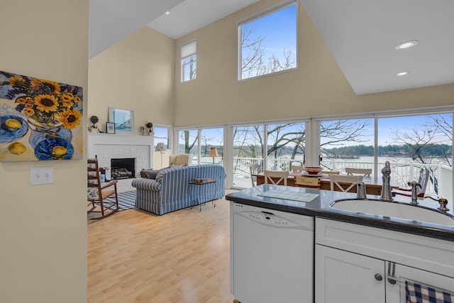 living room featuring recessed lighting, a high ceiling, light wood-style floors, a brick fireplace, and a water view