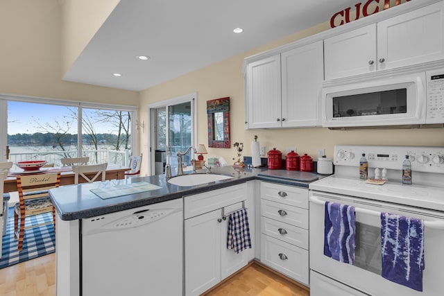 kitchen with white appliances, a peninsula, light wood-type flooring, white cabinets, and a sink