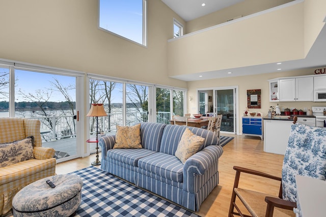 living room with a water view, light wood finished floors, a high ceiling, and recessed lighting