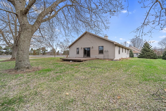 back of property with a deck, a chimney, and a lawn