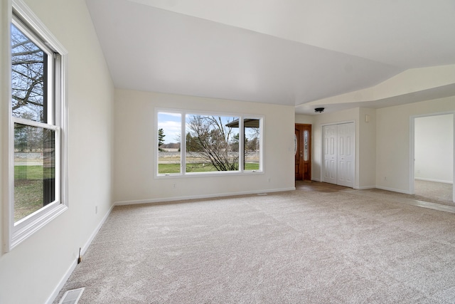 empty room featuring a wealth of natural light, light colored carpet, and lofted ceiling