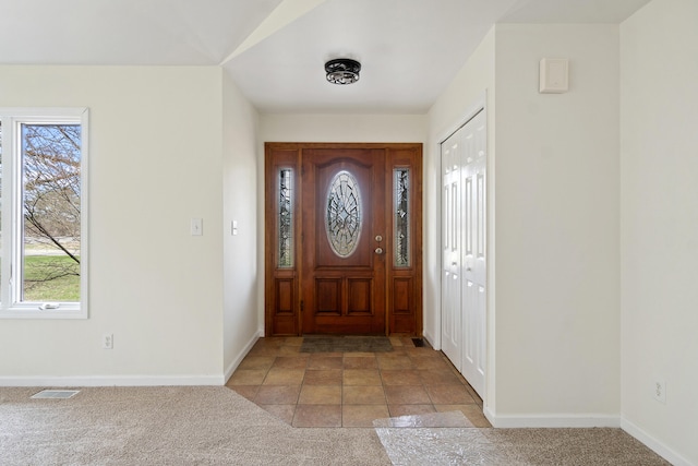 foyer entrance featuring visible vents, baseboards, light colored carpet, and a healthy amount of sunlight