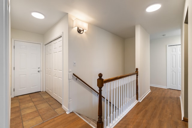corridor featuring wood finished floors, baseboards, and an upstairs landing