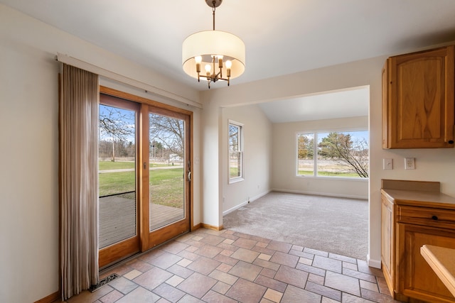 doorway featuring a chandelier, light carpet, stone finish floor, and baseboards