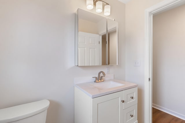 half bathroom with toilet, wood finished floors, vanity, and baseboards