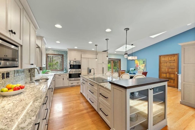 kitchen featuring an island with sink, light wood-style flooring, a sink, built in appliances, and backsplash