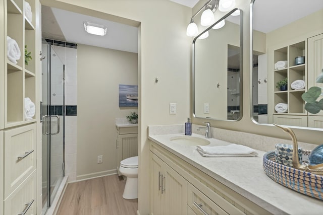 bathroom with toilet, vanity, a stall shower, and wood finished floors