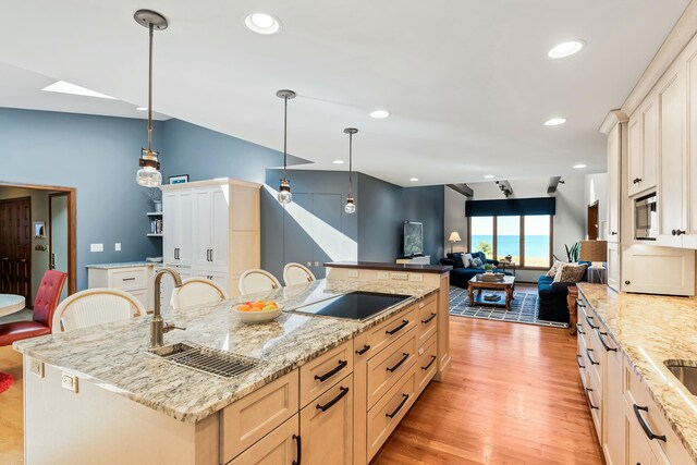 kitchen with stainless steel microwave, black electric cooktop, light wood finished floors, pendant lighting, and a sink