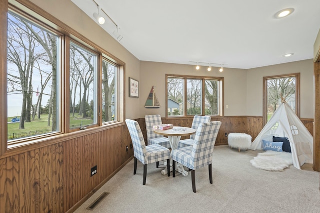 dining space with carpet, track lighting, visible vents, a wainscoted wall, and wood walls