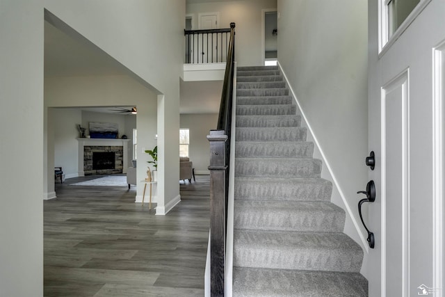 stairs with baseboards, a fireplace, a high ceiling, ceiling fan, and wood finished floors