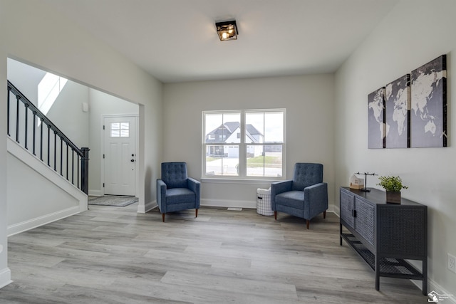 living area with light wood-style floors, baseboards, and stairs