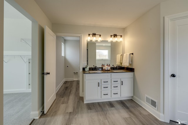 bathroom with wood finished floors, double vanity, a sink, and visible vents