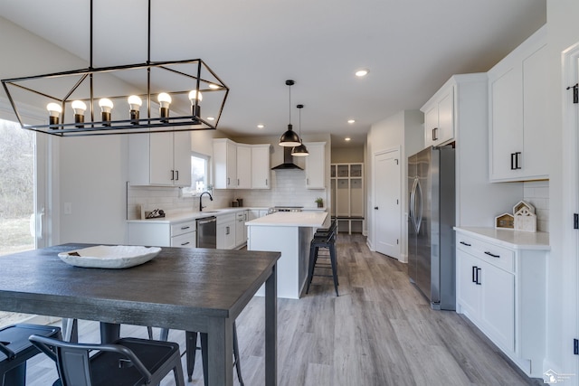 kitchen with wall chimney exhaust hood, a kitchen bar, a chandelier, a center island, and appliances with stainless steel finishes
