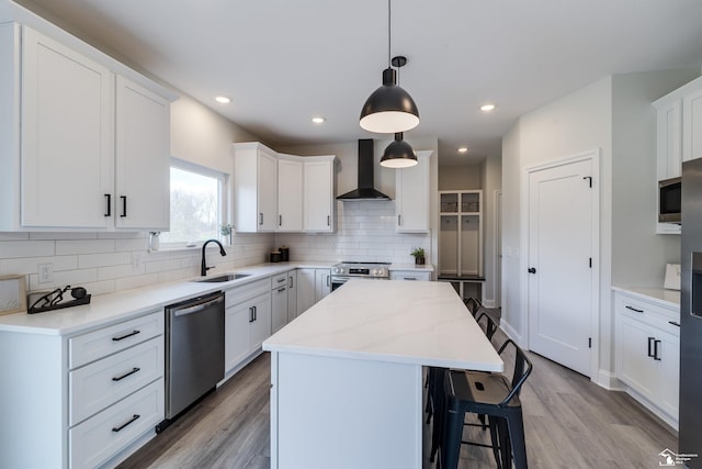 kitchen featuring tasteful backsplash, a center island, wall chimney range hood, appliances with stainless steel finishes, and light wood finished floors