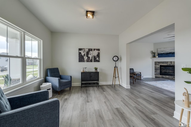 sitting room with a stone fireplace, light wood-style flooring, and baseboards