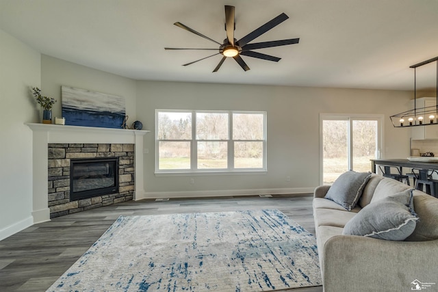 living area featuring baseboards, wood finished floors, a fireplace, and ceiling fan with notable chandelier