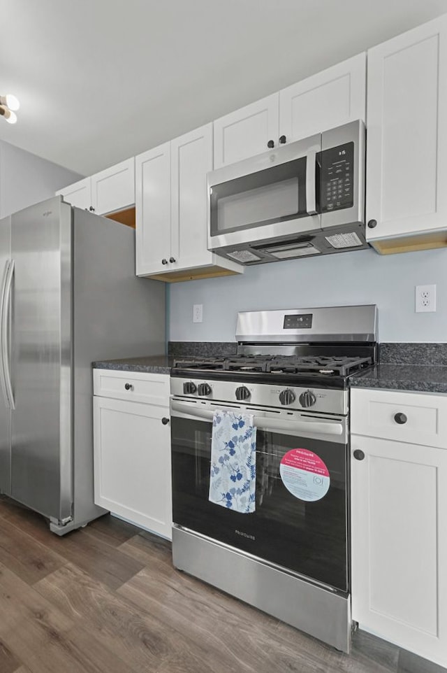 kitchen featuring stainless steel appliances, white cabinetry, dark stone counters, and dark wood-style flooring