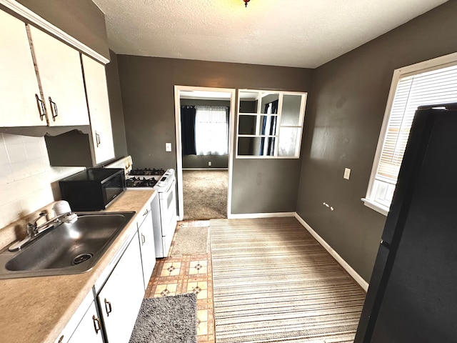 kitchen with black microwave, gas range gas stove, light countertops, a sink, and white cabinetry