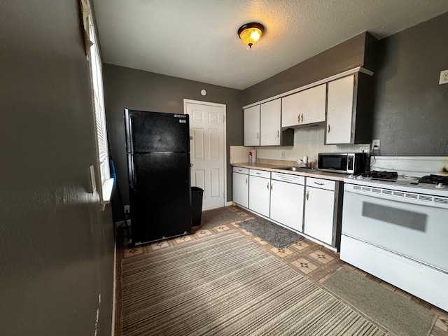 kitchen featuring white gas stove, a sink, light countertops, freestanding refrigerator, and stainless steel microwave