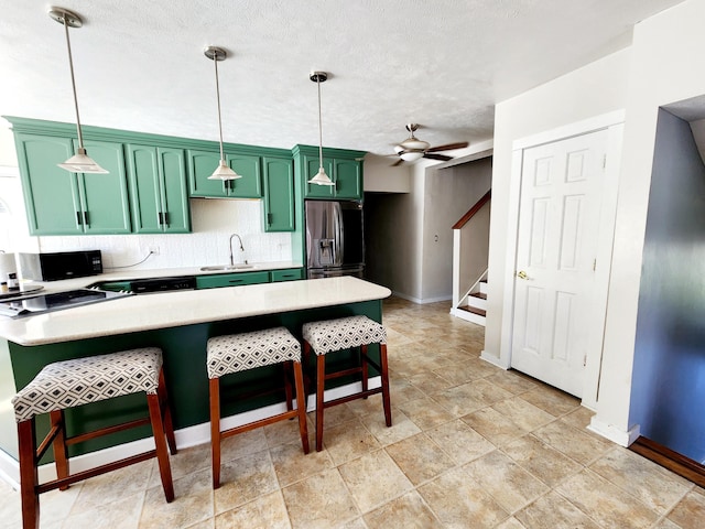 kitchen featuring stainless steel fridge with ice dispenser, a kitchen breakfast bar, light countertops, a sink, and green cabinetry