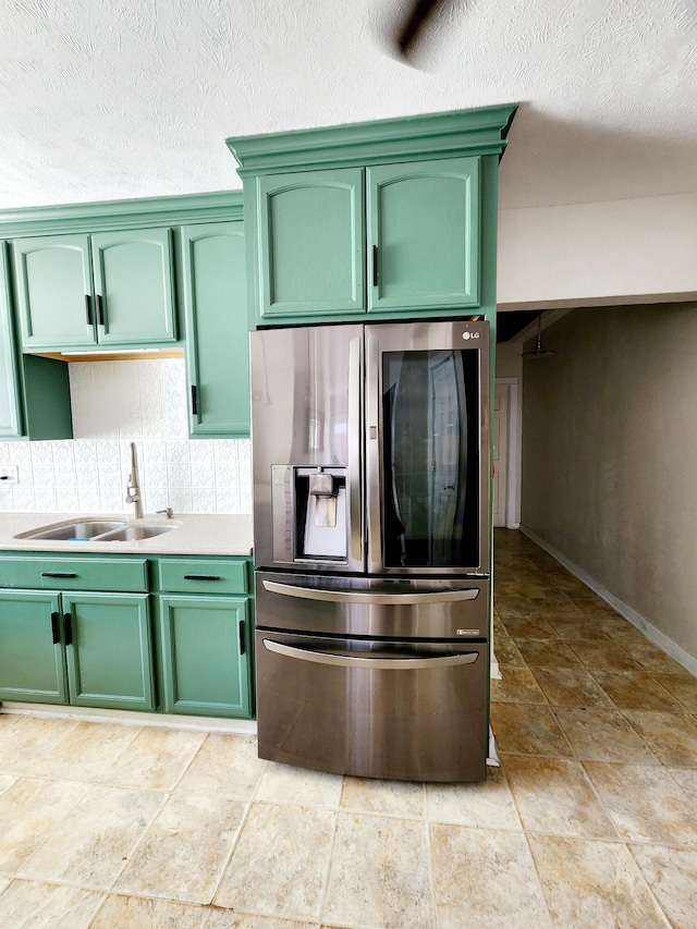 kitchen featuring stainless steel fridge, backsplash, stone tile flooring, green cabinetry, and a sink