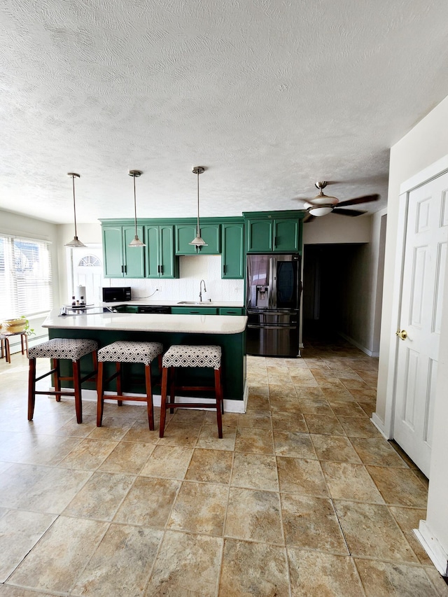 kitchen with green cabinets, a ceiling fan, stainless steel refrigerator with ice dispenser, light countertops, and decorative backsplash