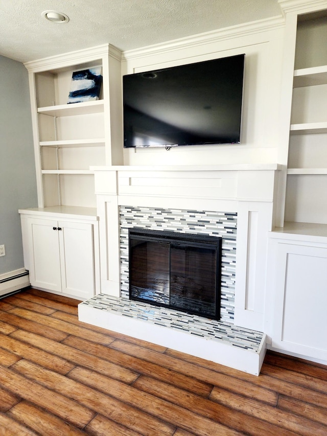 details featuring a textured ceiling, wood finished floors, a tiled fireplace, and built in shelves