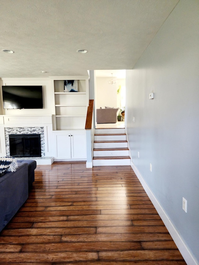 unfurnished living room featuring dark wood-type flooring, a textured ceiling, stairway, a tiled fireplace, and baseboards